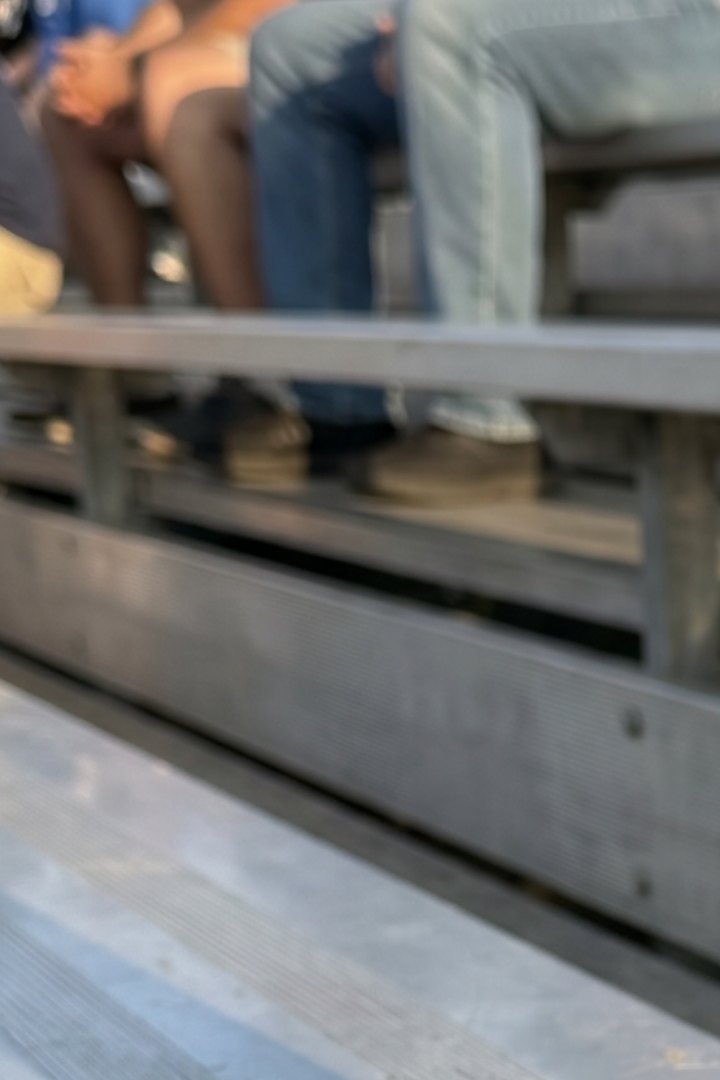 The row above on an aluminum grandstand: sneakers on the footboard, the flat seat plank, and the open gap between footboard and seatboard.